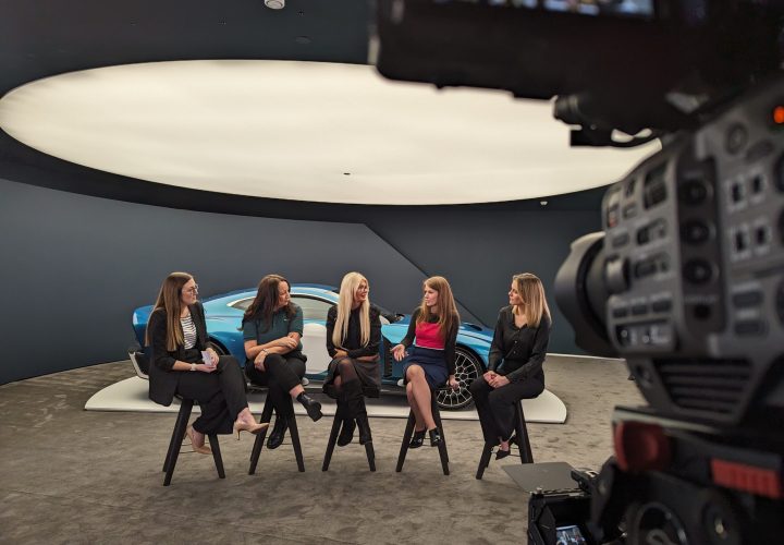 Panel discussion with five women seated in front of a sports car, filmed for a Milton Keynes video production service